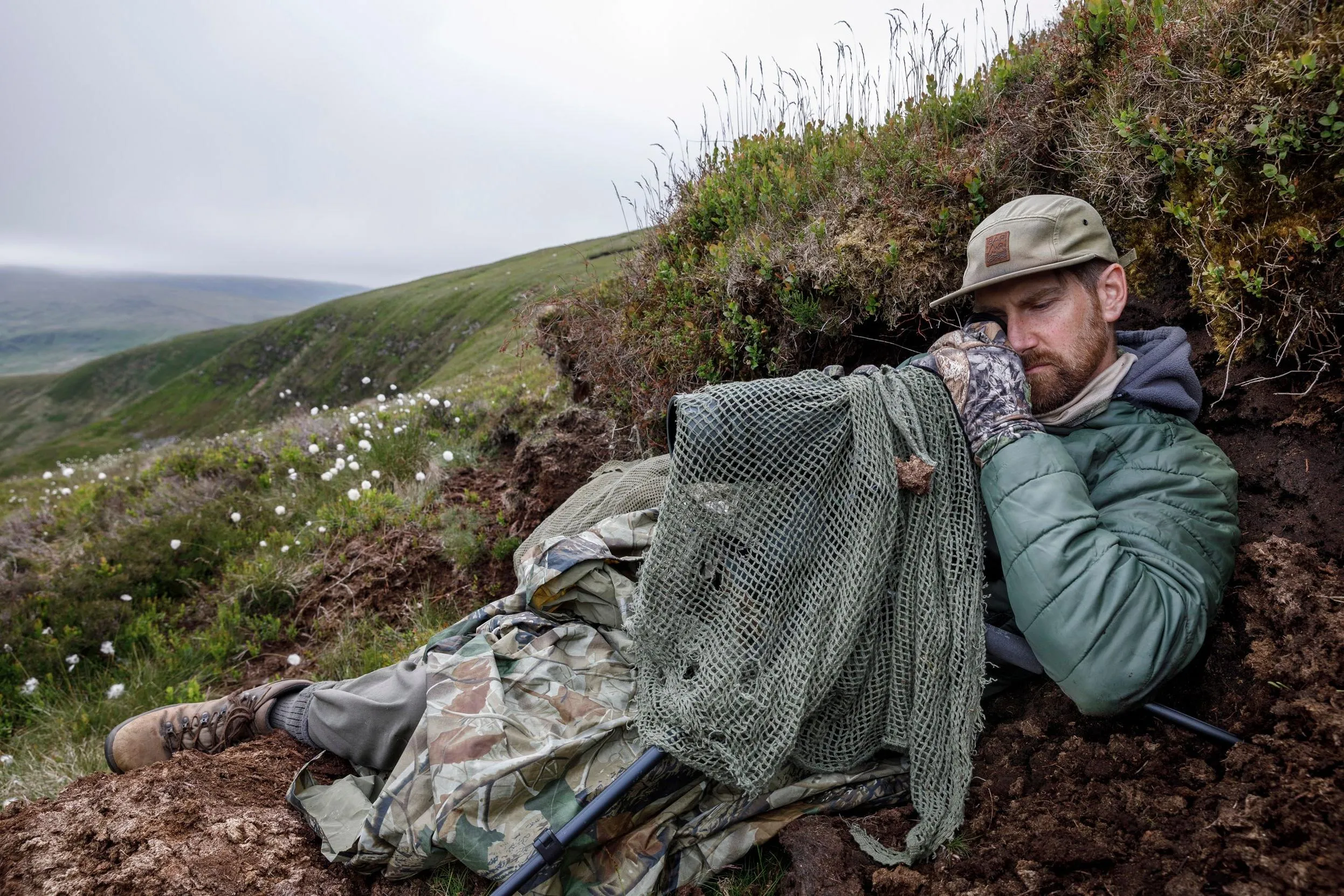 An RSPB staff member hiding in the hillside looking through binoculars.